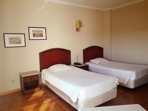 A hotel room with two single beds, a nightstand, a lamp, and two framed pictures on the wall.