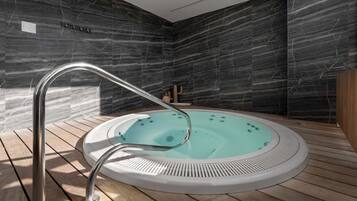Banheira de hidromassagem moderna em ambiente interno, com deck de madeira, em frente a paredes de mármore escuro.