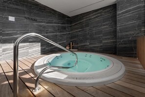 Un jacuzzi intérieur moderne, doté d’une terrasse en bois, installé devant un mur de marbre sombre.