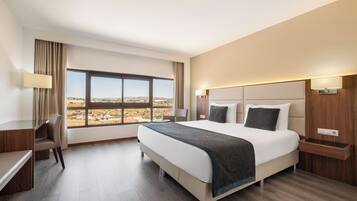 A hotel room with a large bed, a desk, and a view of a landscape.