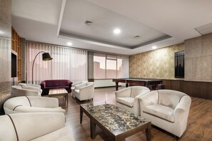 Un área de estar moderna con mesa de billar, asientos cómodos y un amplio ventanal con vista a la ciudad.