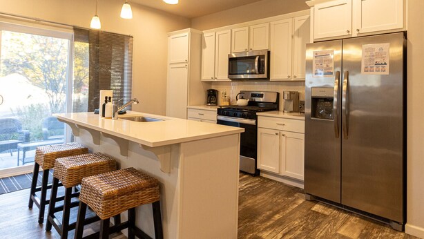 A modern kitchen with white cabinets, stainless steel appliances, and a central island with stools. - Harbor Pointe - Modern, Close to Lake Michigan! (South Haven)