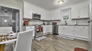 Una cocina moderna con armarios blancos, electrodomésticos de acero inoxidable y un comedor con una mesa preparada para dos.
