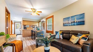 A modern living room with a brown leather sofa, a round wooden coffee table, and a ceiling fan. - Fishing · Kayaks · Firepit · Paddleboat (Pierceton)