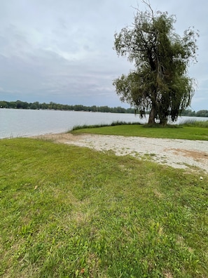 Escape to a serene lakeside haven with a tranquil tree-lined shore and a peaceful grassy area perfect for leisurely strolls.
