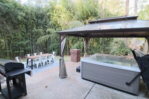 An outdoor patio with a hot tub, grill, and dining area. - Classic City Retreat in Five Points, Athens GA | Theater | Hot Tub | Christmas (Athens)