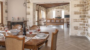 A dining area with a stone wall, wooden furniture, and a fireplace. - Villa Aloe (Pitsidia)