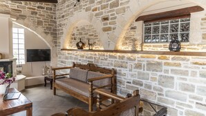 A stone-walled room with a wooden bench, a television, and a window with a view. - Villa Aloe (Pitsidia)