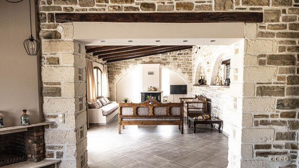 A stone-walled room with a fireplace, a sofa, and a wooden bench. - Villa Aloe (Pitsidia)