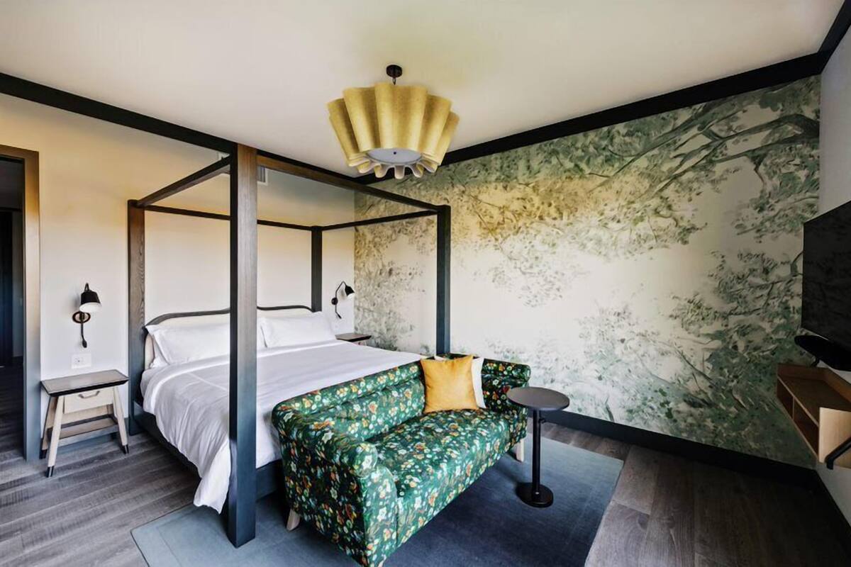 A four-poster bed with a green floral sofa, a small round table, and a wall with a nature mural.