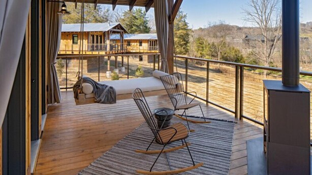 Una terraza de madera con un sofá, sillas, una chimenea y vistas a cabañas al fondo.