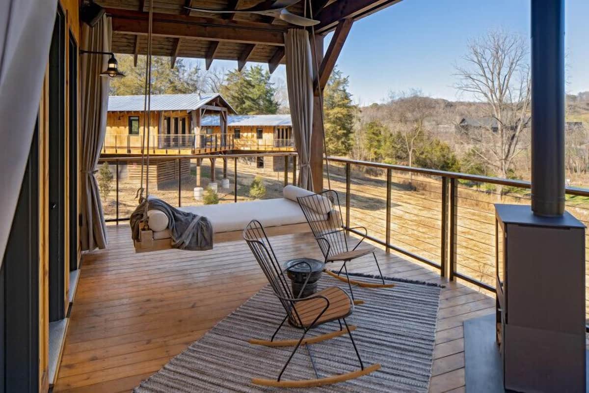 A wooden deck with a sofa and chairs, a fireplace, and a view of cabins in the background.