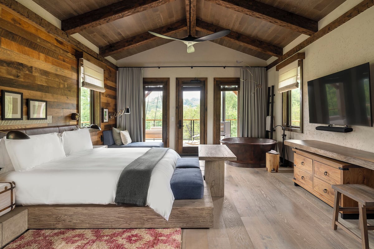 A spacious bedroom with a large bed, a wooden ceiling, a bathtub, and a TV.