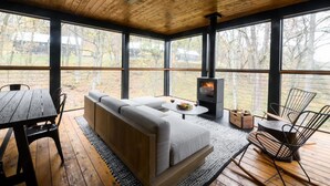 Una habitación acogedora con techo de madera, ventanas amplias, un sofá, una mesa y un estufa de leña.