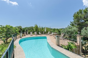Piscina com borda curva, cercada por grade, adjacente a um espaço de estar com cadeiras e mesas.