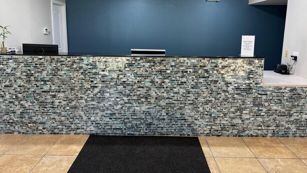 A reception area with a dark blue wall, a mosaic tile counter, and a black rug. - Executive Inn and Suites Baker (Baker)