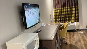 A compact kitchenette with a microwave, a small refrigerator, and a flat-screen TV displaying a tennis match. - Executive Inn and Suites Baker (Baker)