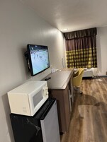 Uma cozinha compacta com micro-ondas, um refrigerador pequeno e uma televisão de tela plana exibindo uma partida de tênis.