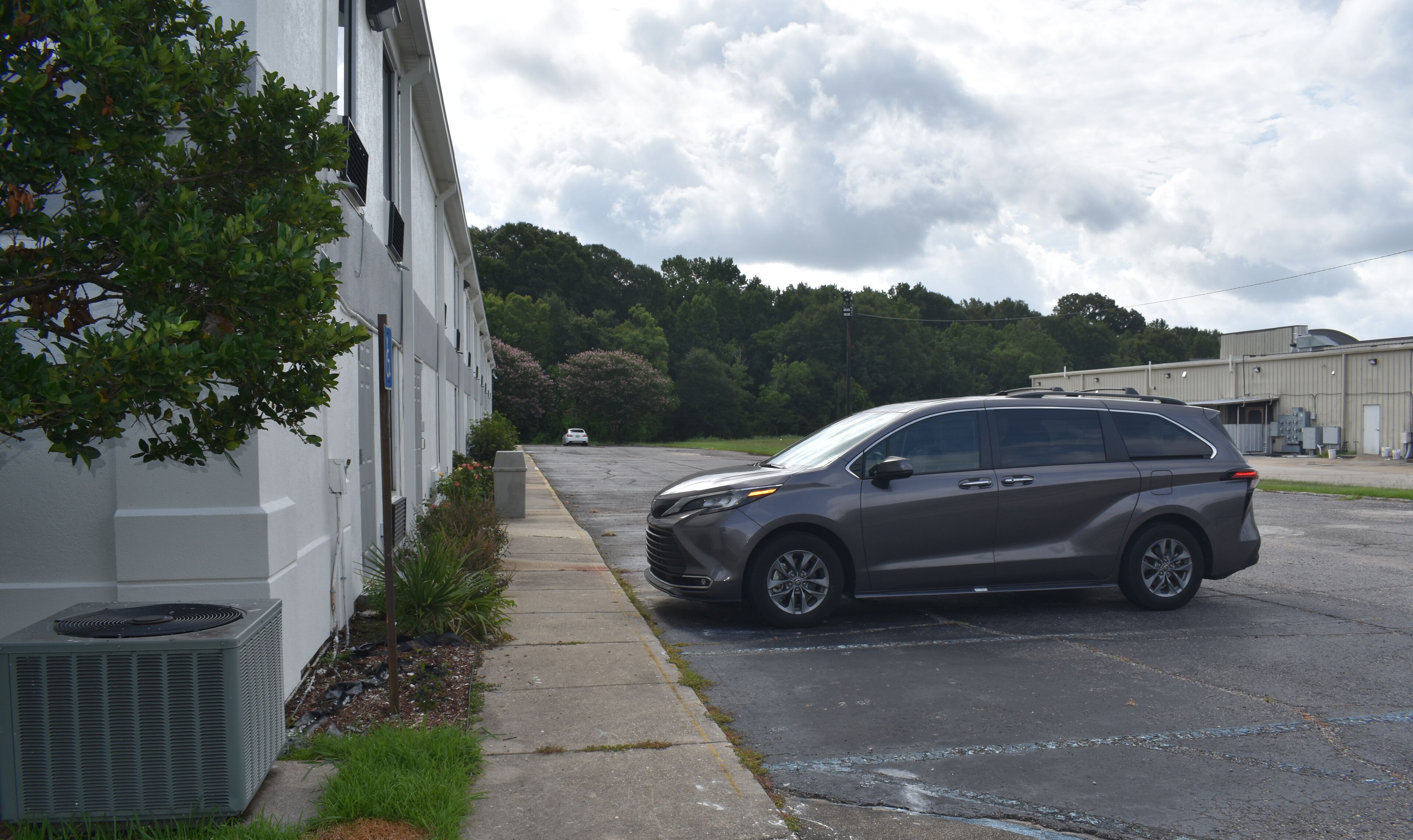 A parking lot with a gray SUV parked near a building with air conditioning units and a tree.