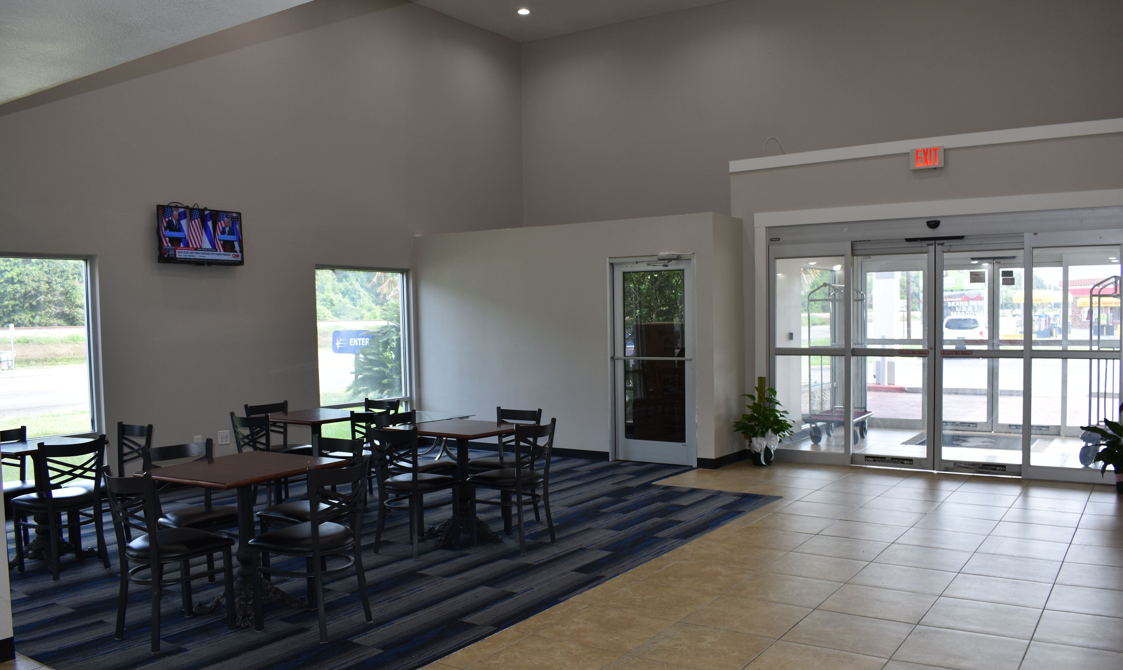 A spacious indoor area with multiple tables and chairs, a large window, and an exit door.