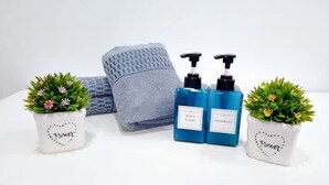 Un baño con una toalla, dos botellas de gel de ducha y dos macetas con la palabra 'Flower'.