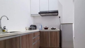 Una cocina compacta con armarios de madera, un lavamanos de acero inoxidable, una campana extractora negra y un refrigerador.
