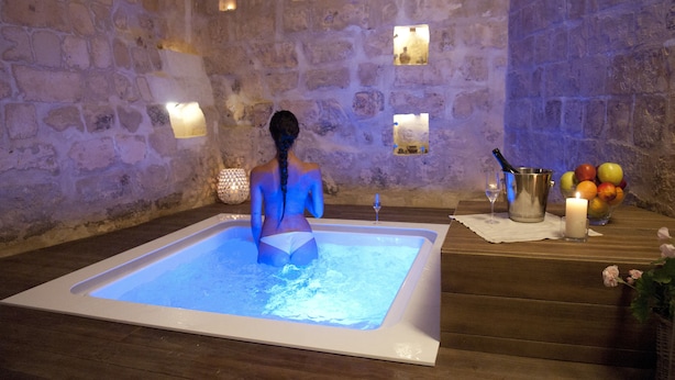 A stone-walled room with a bathtub, candles, fruit, and a wine glass. - MATA SUITE (Matera)
