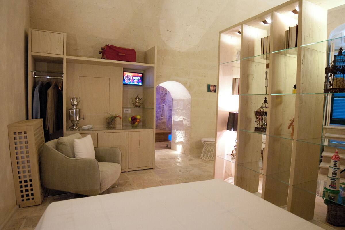 Habitación de hotel con cama, zona de estar, televisor y separador de vidrio.