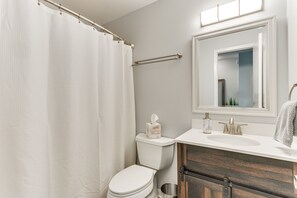 A bathroom with a white toilet, a wooden vanity, a mirror, and a shower curtain. - 10 Mi to Navarre Beach! Waterfront Rental w/ Pool (Mary Esther)