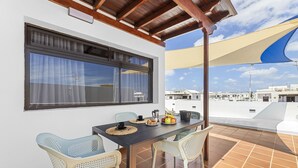 A terrace with a table set for breakfast, two chairs, a window with curtains, and a view of other buildings. - La casa de las velas (Playa Honda)