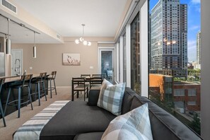 Um apartamento moderno com área de jantar, sofá com almofadas e amplas janelas com vista para a cidade.