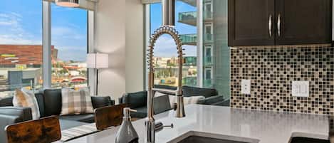 A modern kitchen with a large island, dark cabinets, and a city view.
