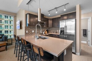 Cozinha moderna com ilha central, eletrodomésticos de aço inoxidável e vista para um edifício residencial.