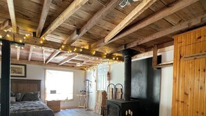A rustic room with a bed, a fireplace, and wooden beams on the ceiling.