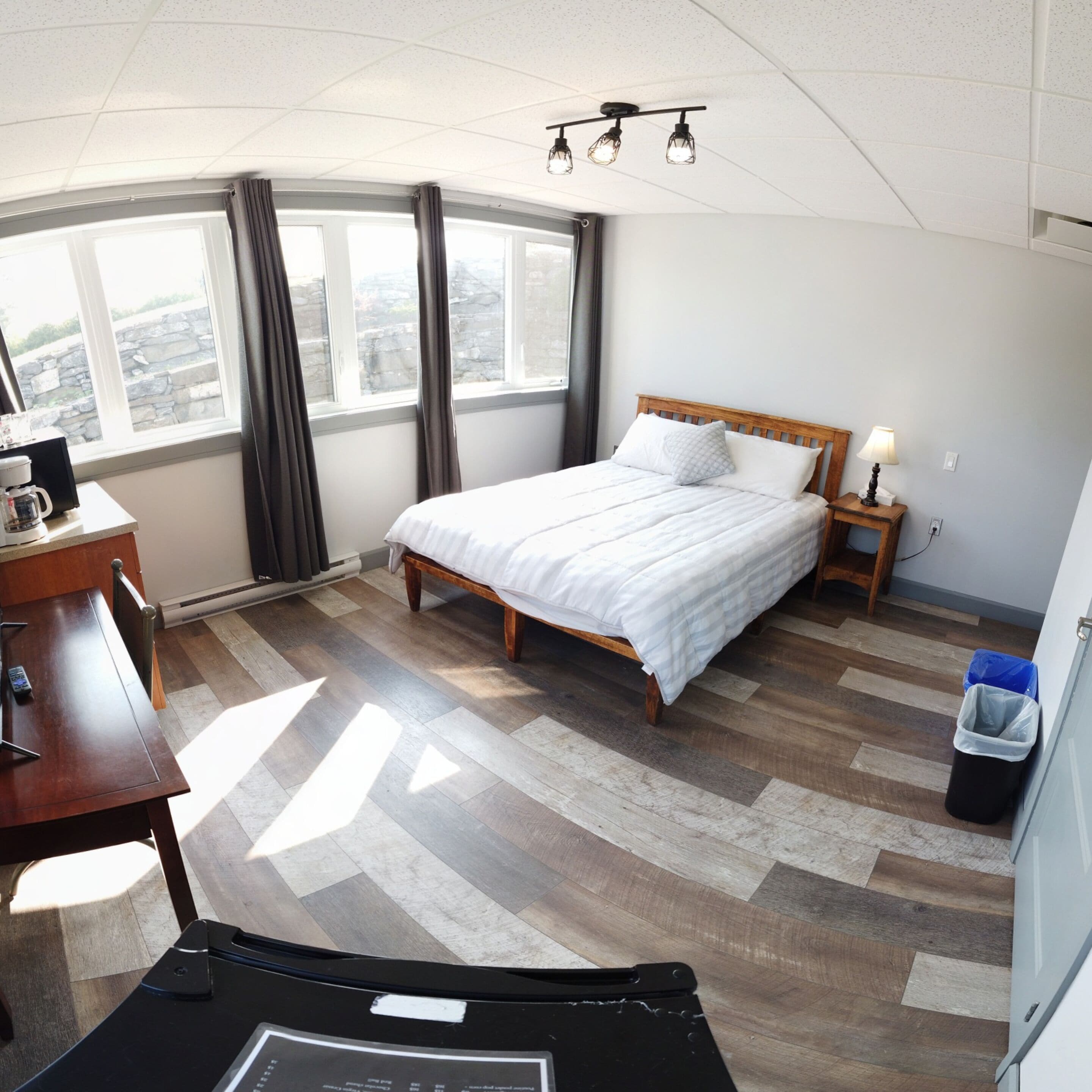 Habitación de hotel con cama, mesita de noche, lámpara y vistas amplias a la ciudad.