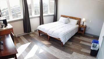 A hotel room with a bed, bedside table, lamp, and a view of the city through large windows.