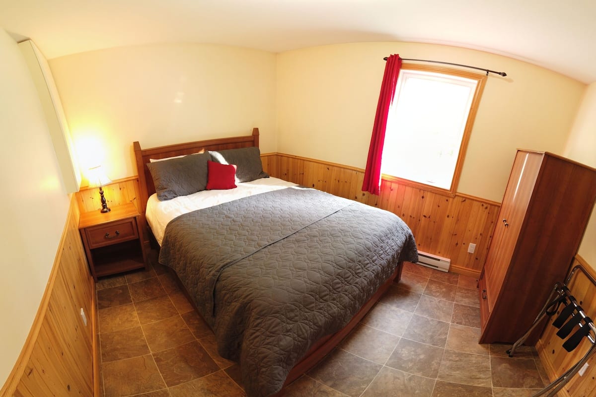 Un dormitorio con cama, armario de madera y ventana con cortinas.