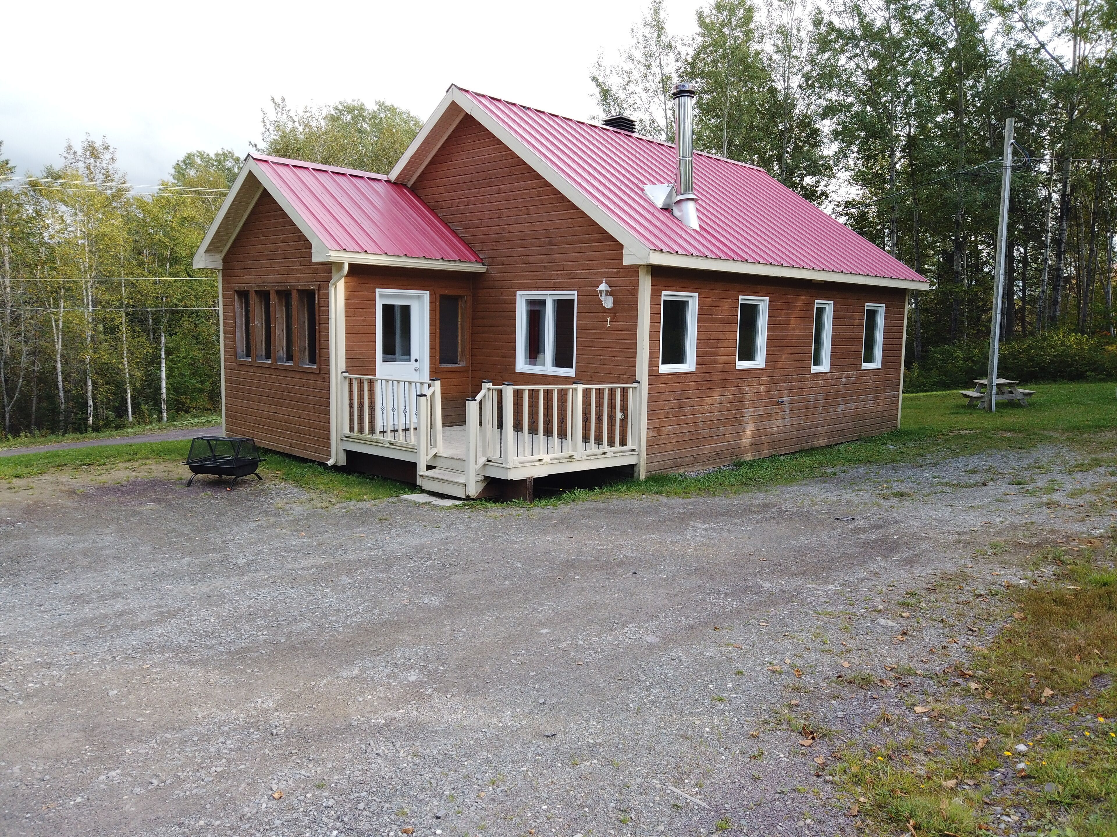 En stuga av trä med ett rött tak, en veranda och en skorsten.