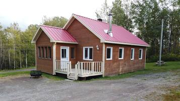 En stuga av trä med ett rött tak, en veranda och en skorsten.