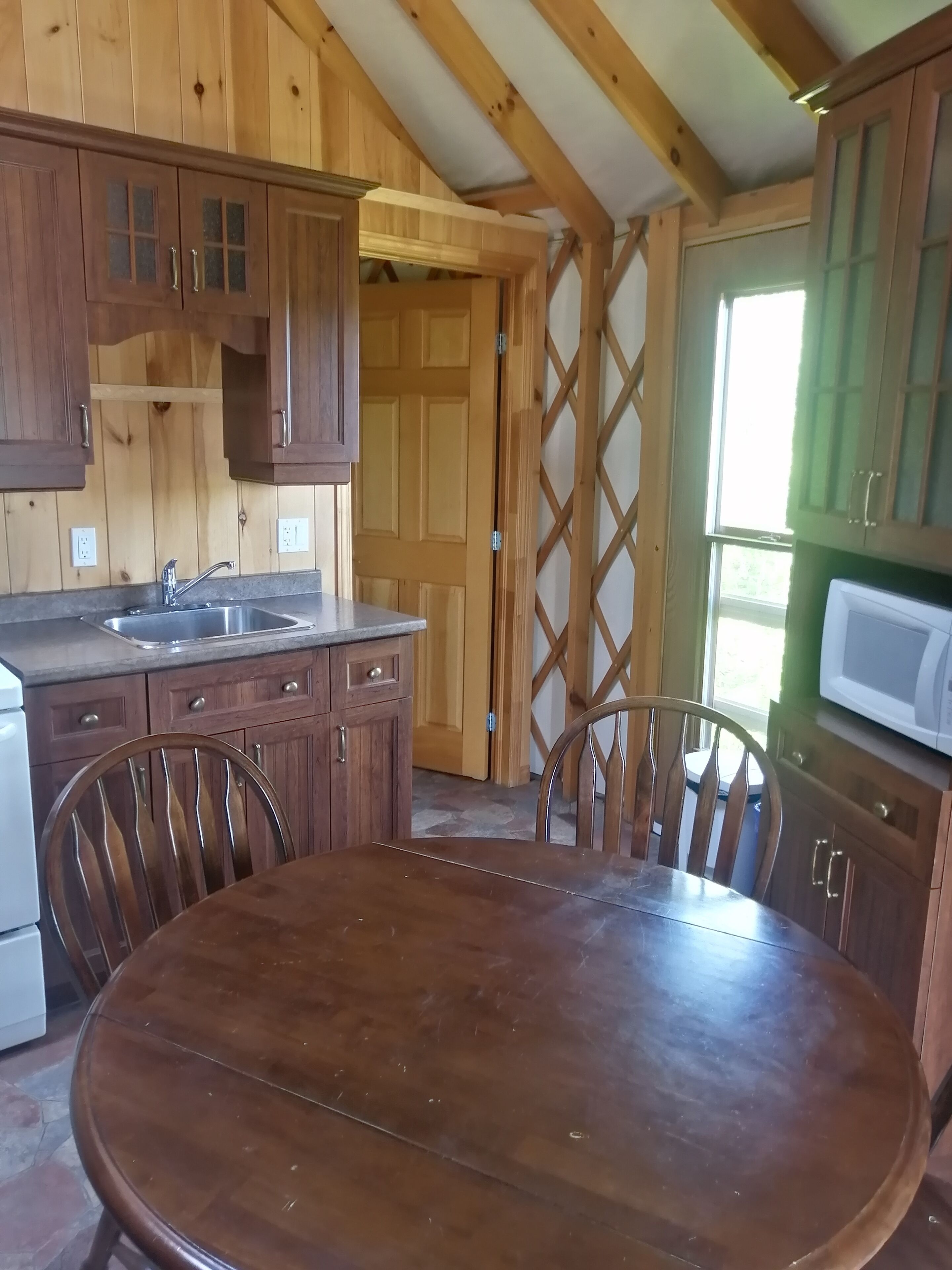 A wooden kitchen with a round table and chairs, a sink, cabinets, and a microwave.