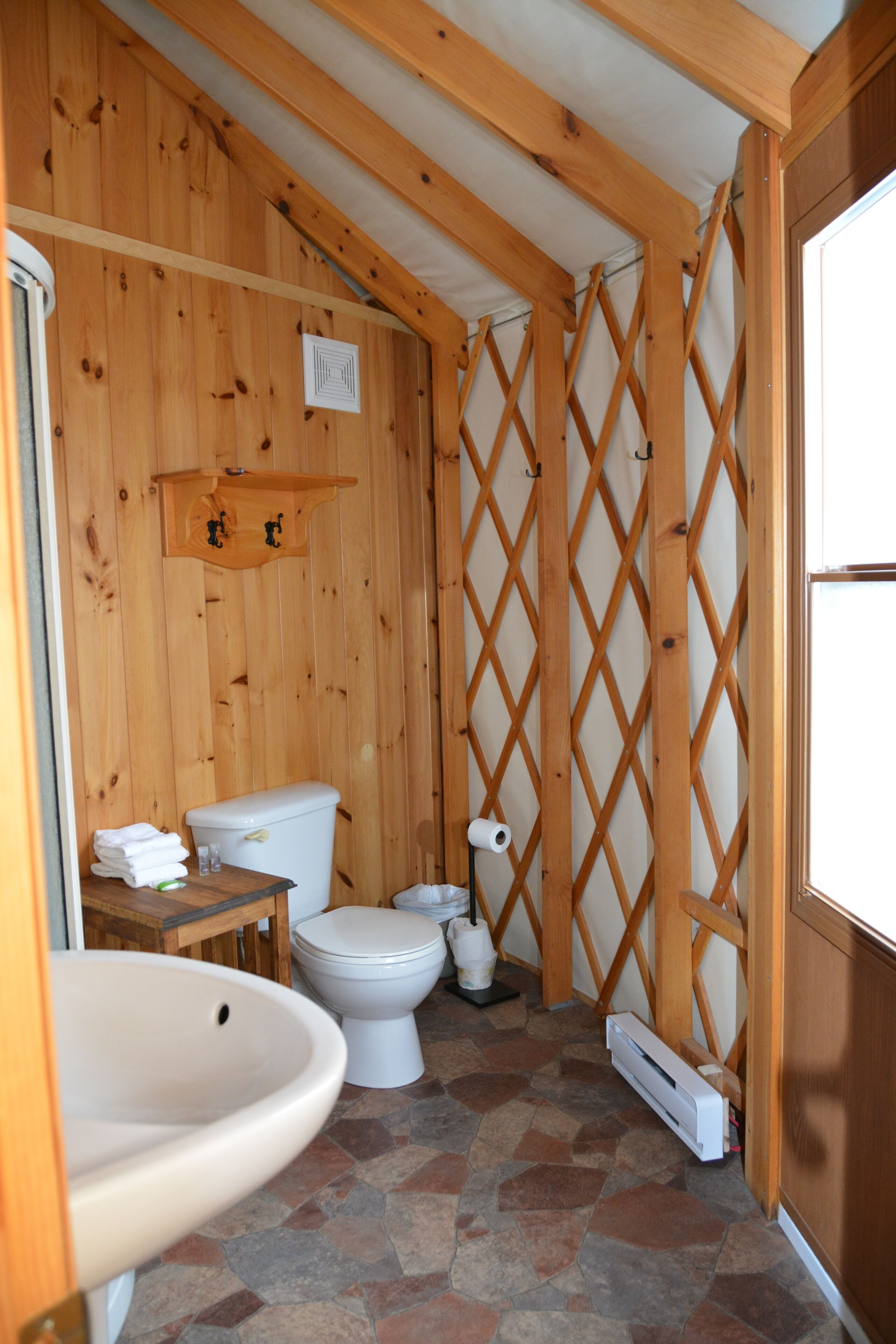 A small, wooden bathroom with a toilet, sink, and shower area.