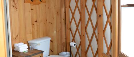 A small, wooden bathroom with a toilet, sink, and shower area.