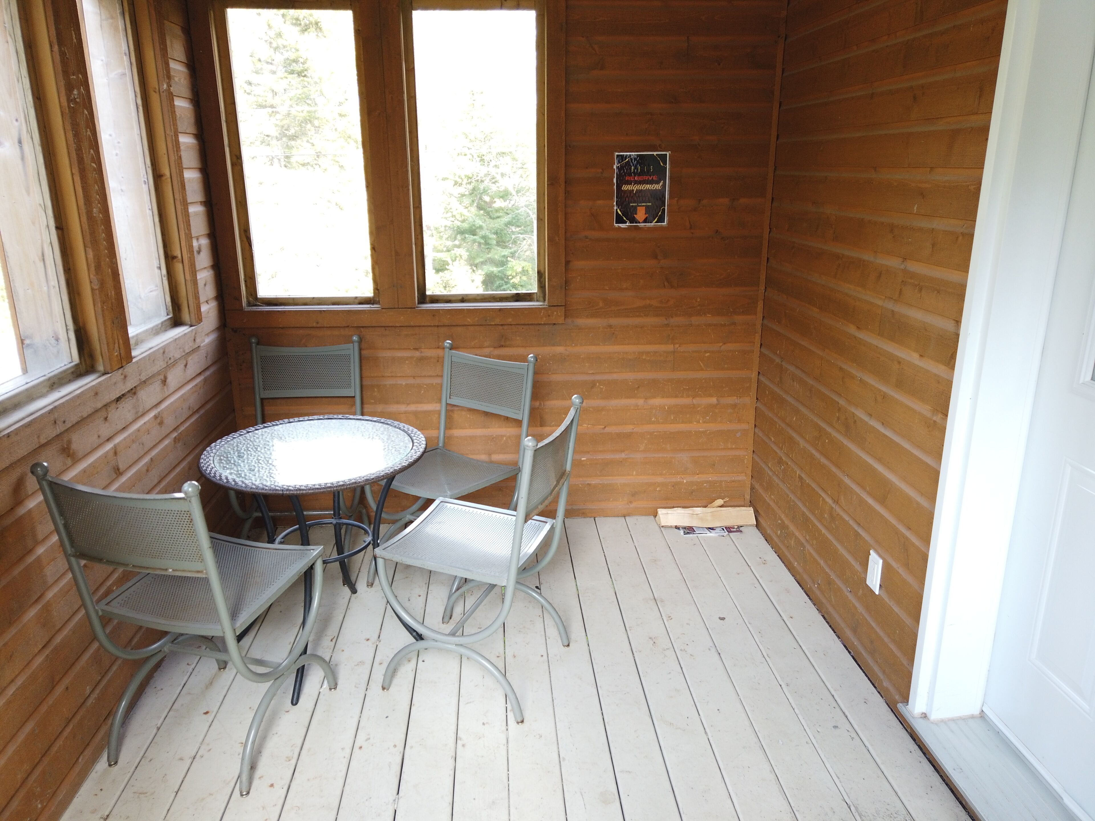 A wooden cabin with a round table and four chairs. There are two windows providing natural light, and a sign on the wall.