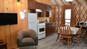 A cozy kitchen with wooden cabinets, a white stove, and a dining area with wooden chairs and a table. - Parc du Mont-Citadelle (Saint-Honoré-de-Témiscouata)