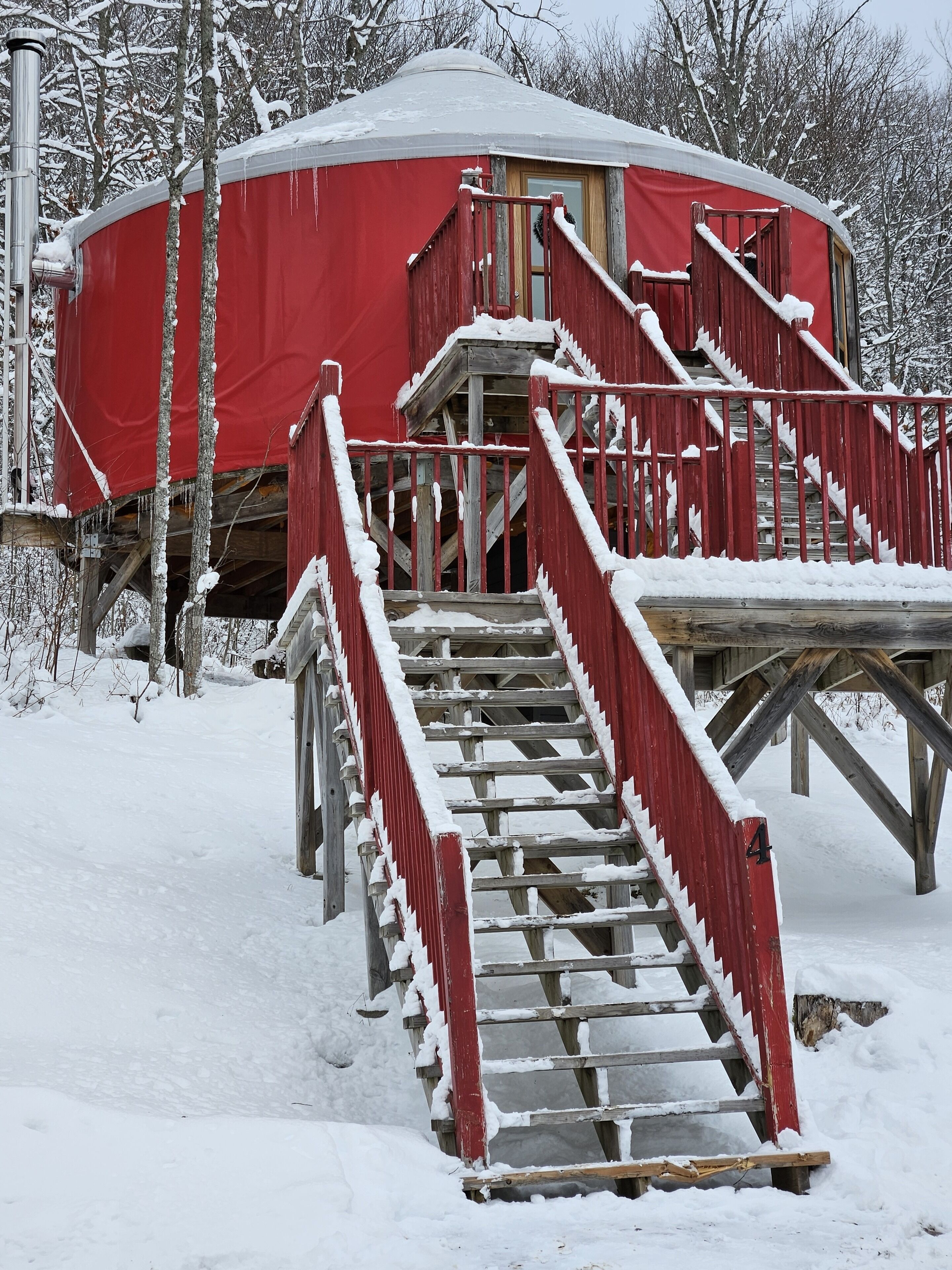 A red yurt with a wooden staircase leading to a door.