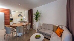 A modern living room with a grey sofa, a dining table with chairs, a coffee table with apples, and a large plant. - Villa Tetra - Six Bedroom Villa, Sleeps 11 (Okrug Gornji)