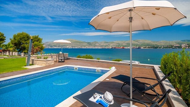 A poolside area with a view of the sea, a lounge chair, and a table with a hat and sunglasses. - Villa Tetra - Six Bedroom Villa, Sleeps 11 (Okrug Gornji)