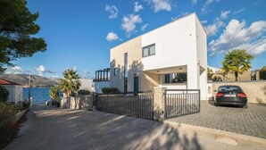 A modern two-story house with a white facade, a paved driveway, and a car parked in the driveway. - Villa Panda - Six Bedroom Villa, Sleeps 11 (Okrug Gornji)