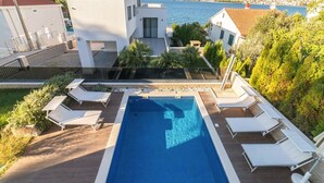 A modern pool area with lounge chairs, a clear view of the sea, and a mountainous backdrop. - Villa Panda - Six Bedroom Villa, Sleeps 11 (Okrug Gornji)