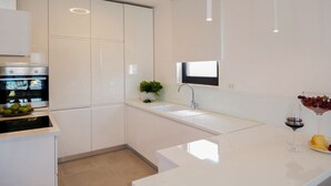 A modern kitchen with white cabinetry, a built-in oven, a sink, and a countertop with a potted plant and a glass of red wine. - Villa Panda - Six Bedroom Villa, Sleeps 11 (Okrug Gornji)